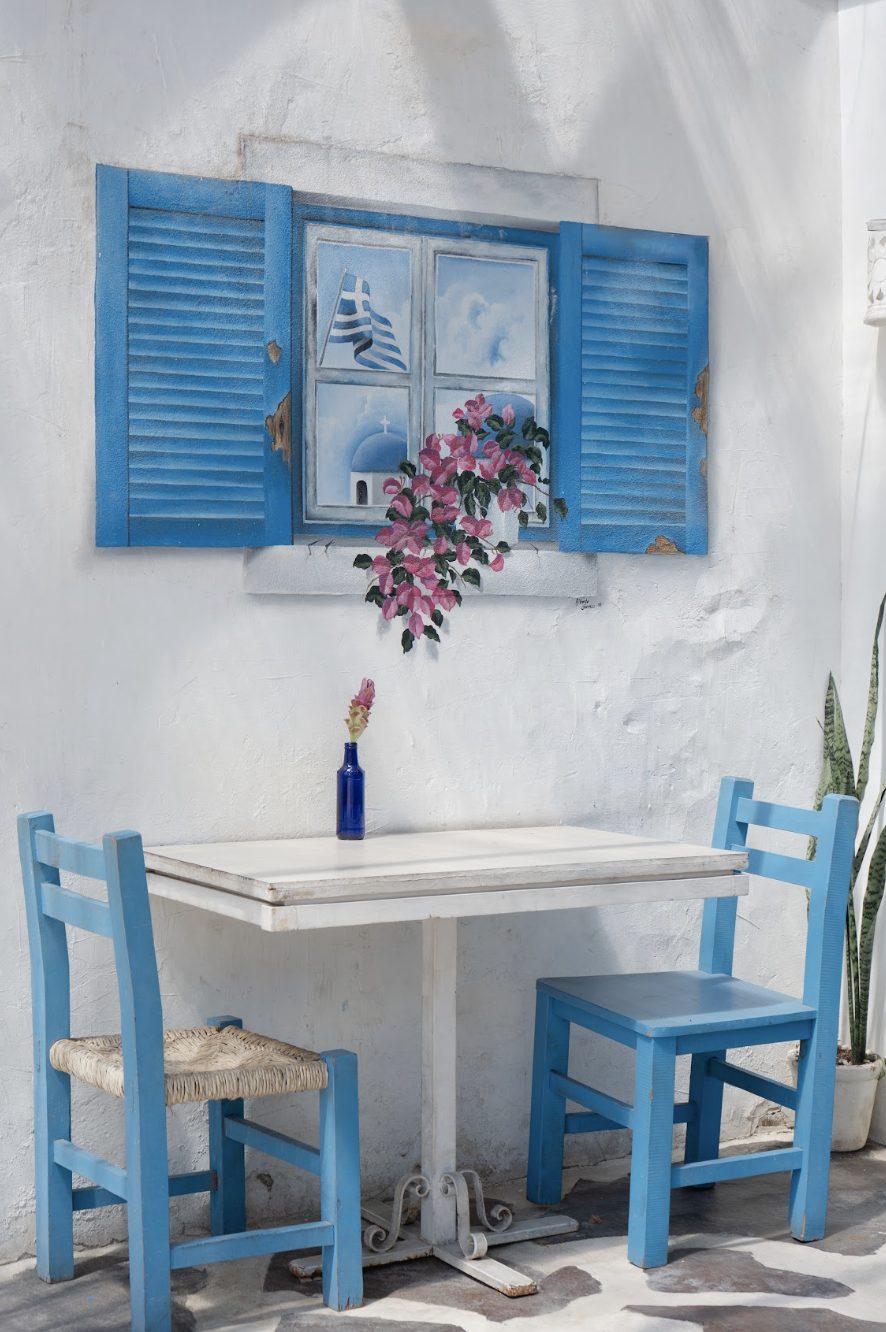 Rincón interior de OPA con mural de ventana griega y mesa azul